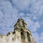 Bell tower of Mission San Juan church with clouds behind it.