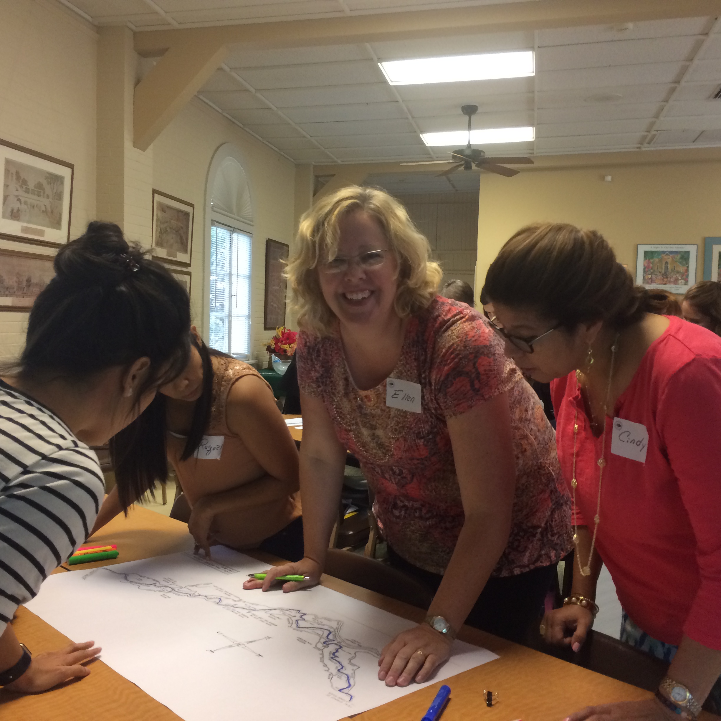 Four teachers, one looking at the camera and smiling, reviewing workshop materials at the Teacher Education Seminar in the River House