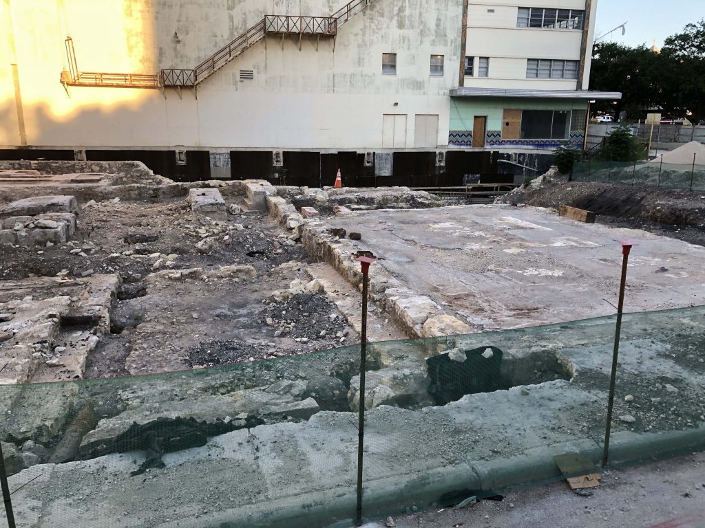 Photo of the uncovered foundation of St. James African Methodist Episcopal church with the Alameda Theater in the background. The cornerstone is wrapped in a black covering.