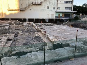 Photo of the uncovered foundation of St. James African Methodist Episcopal church with the Alameda Theater in the background. The cornerstone is wrapped in a black covering.