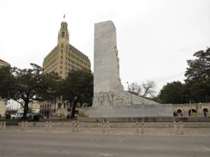 West side of the Alamo Cenotaph with the walls of the Long Barrack and the Emily Morgan Hotel in the background.