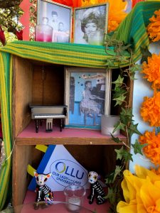 Left side of the Mary Andrews ofrenda includes photos, a mini piano, and pet figurines
